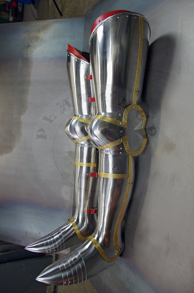 English style leg harness with fully closed cuisses, full greaves with characteristic line around outside ankles. Demi-greaves connected with greaves on rotary pin. Made of medium carbon steel of various thickness from 1 mm up to 1,5 mm. Heat hardened and tempered up to 42 HRC. Brass bands decoration motive based on example visible on Henry V tournament helm. Hand made steel buckles in set./Osony ng w stylu angielskim z w peni zamknitymi nabiodrkami, nagolennicami z charakterystyczn lini wok zewntrznej kostki. Demi-greave poczony z nagolennicami poprzez obrotowy pin. Wykonane ze stali redniowglowej rnej gruboci od 1 mm do 1,5 mm. Hartowane i odpuszczane do 42 HRC. Mosine listwy dekoracyjne z motywem wzorowanym na hemie turniejowym Henryka V. W zestawie rcznie robione sprzczki stalowe.